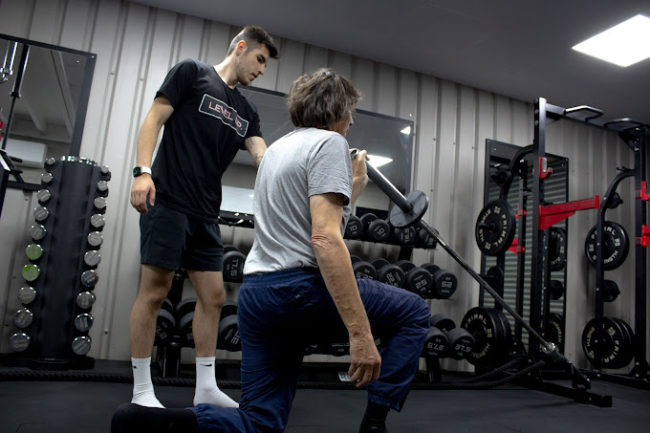 Client kneeling and holding weight for a mobility class, Instructor is assisting and supervising