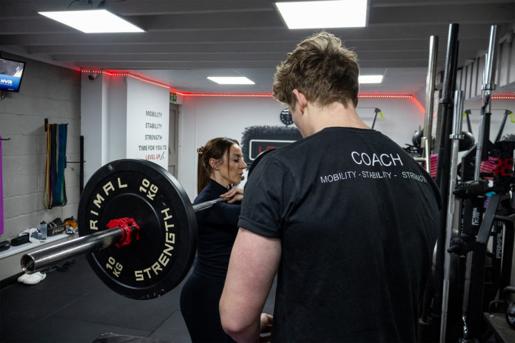 Coach assisting female client with a barbell