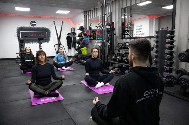 Instructor teaching a yoga class for four female clients, everyone is sitting crossed legged on their yoga mats