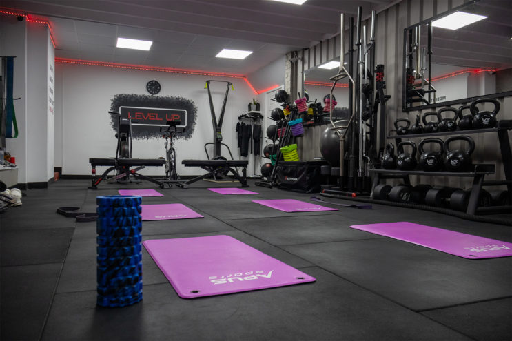 Main gym space: Purple yoga mats on the floor, a foam roller and free weights lined up along the side of the wall