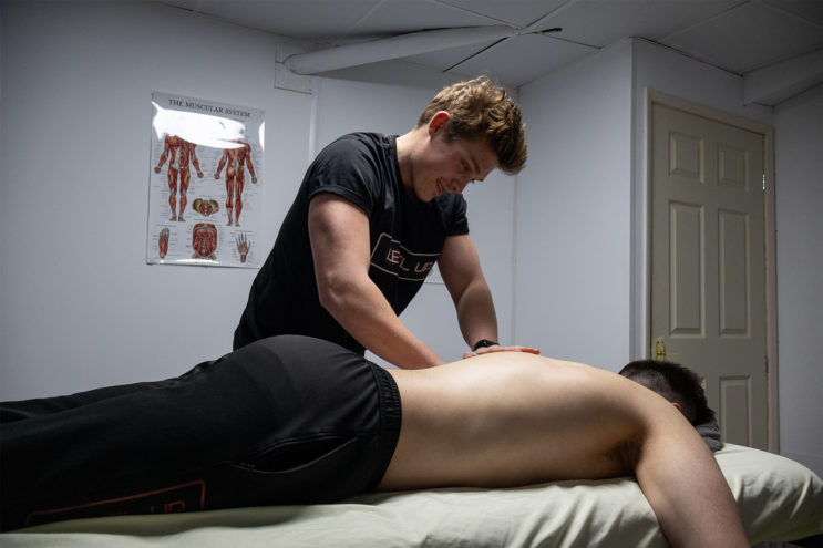 Client receiving a massage from an instructor with a poster of the human muscle system in the background