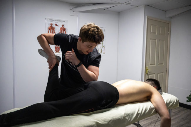 Client receiving a sports massage from an instructor. The client is having their leg raised and bent while on the massage table