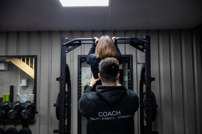 Client being supported with pull ups, the coach is standing behind her - holding her back.